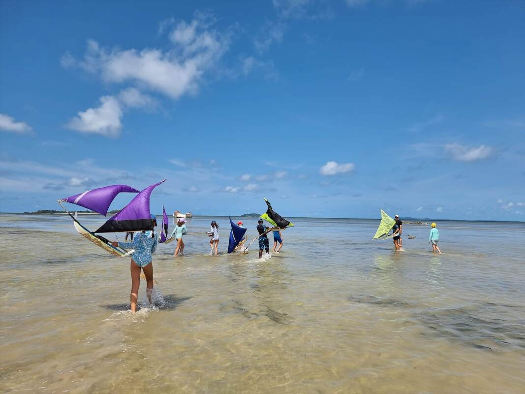 Kids wading out with purple, black and lime jong sails across a wide shallow flat