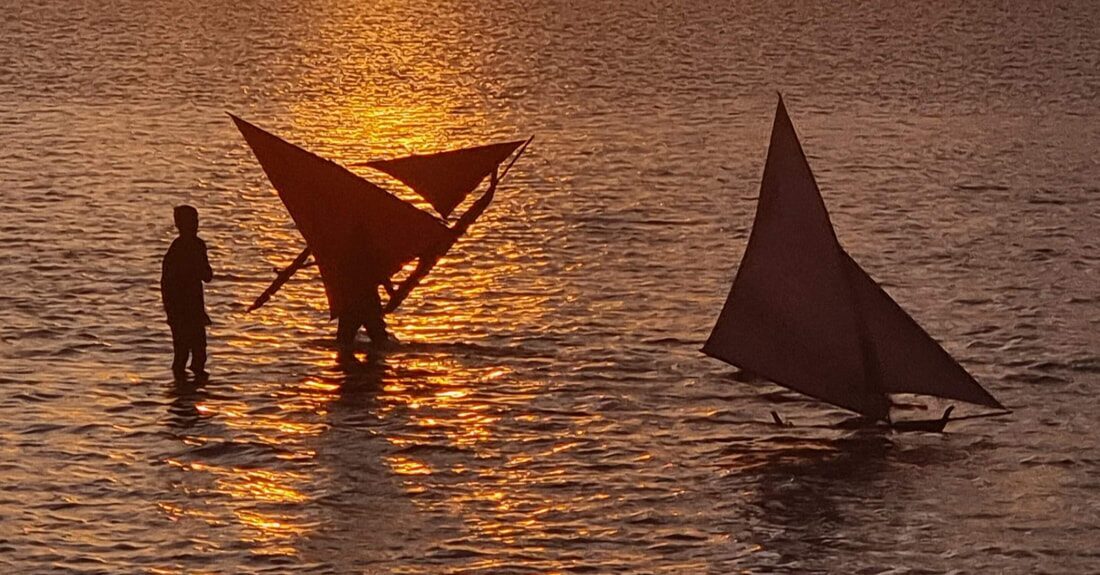 Jongs on the beach at dusk, sails silhouetted against an amber sunset