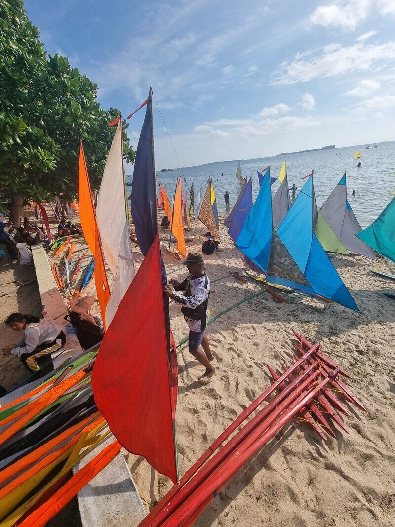 A crowd gathered around a lineup of colorful jong sails on the beach