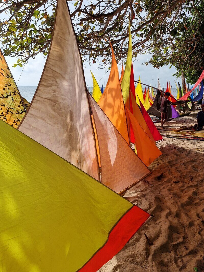 A jong with an orange and yellow sail resting on the beach