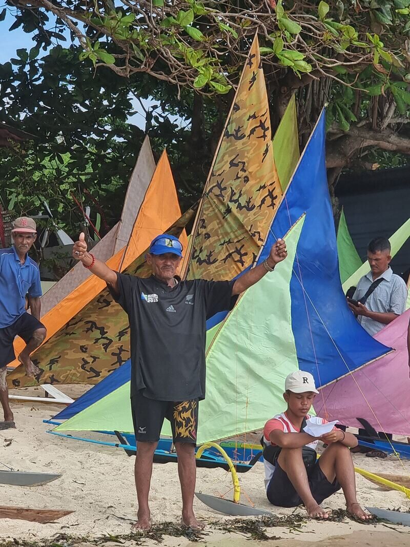 A group of men standing together, several holding jong sail spars