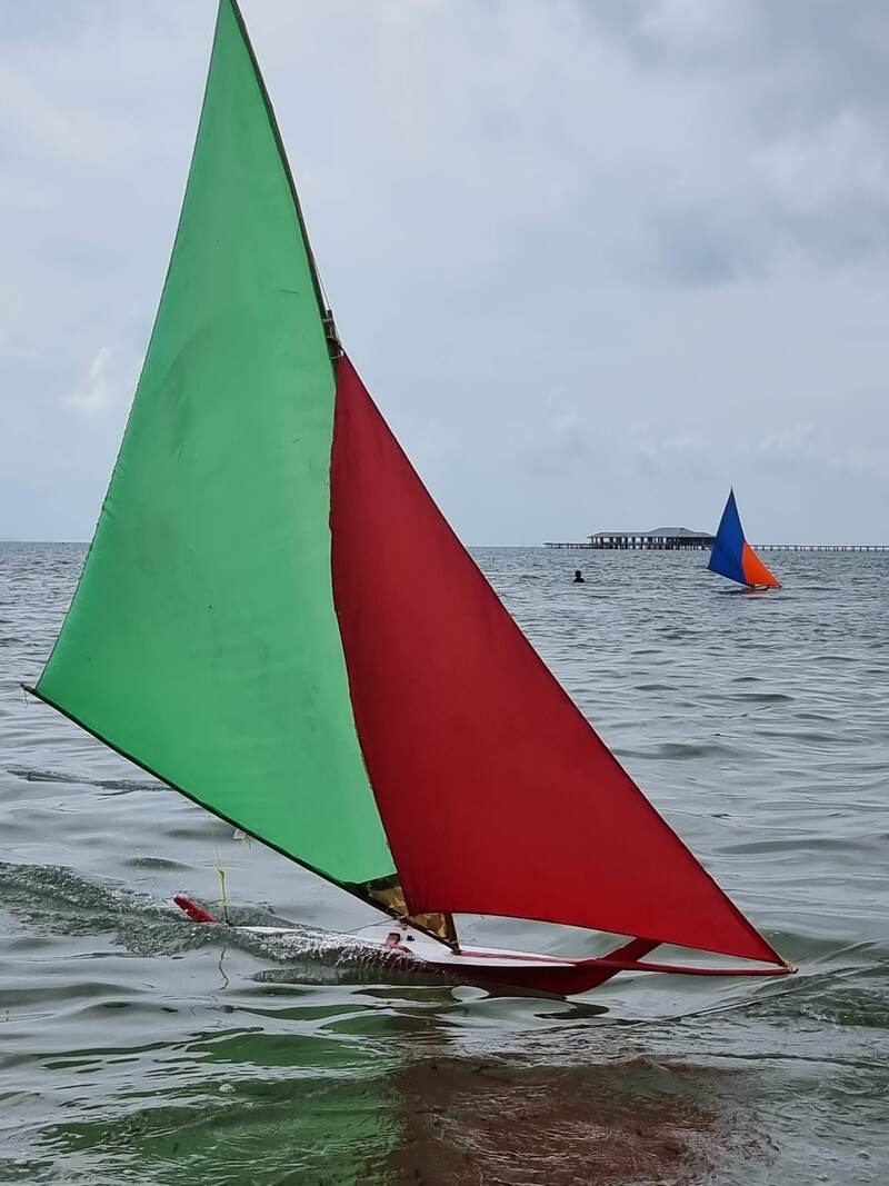 A green and red jong sail on the beach, people gathered nearby