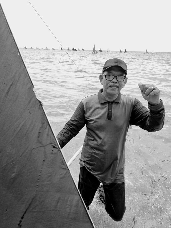 Black-and-white photo of a man kneeling and working on the sand