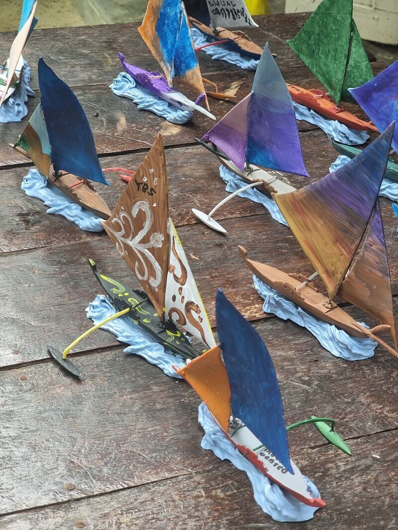 A tabletop crowded with small hand-painted wooden jong models in blue, purple, orange and green sails