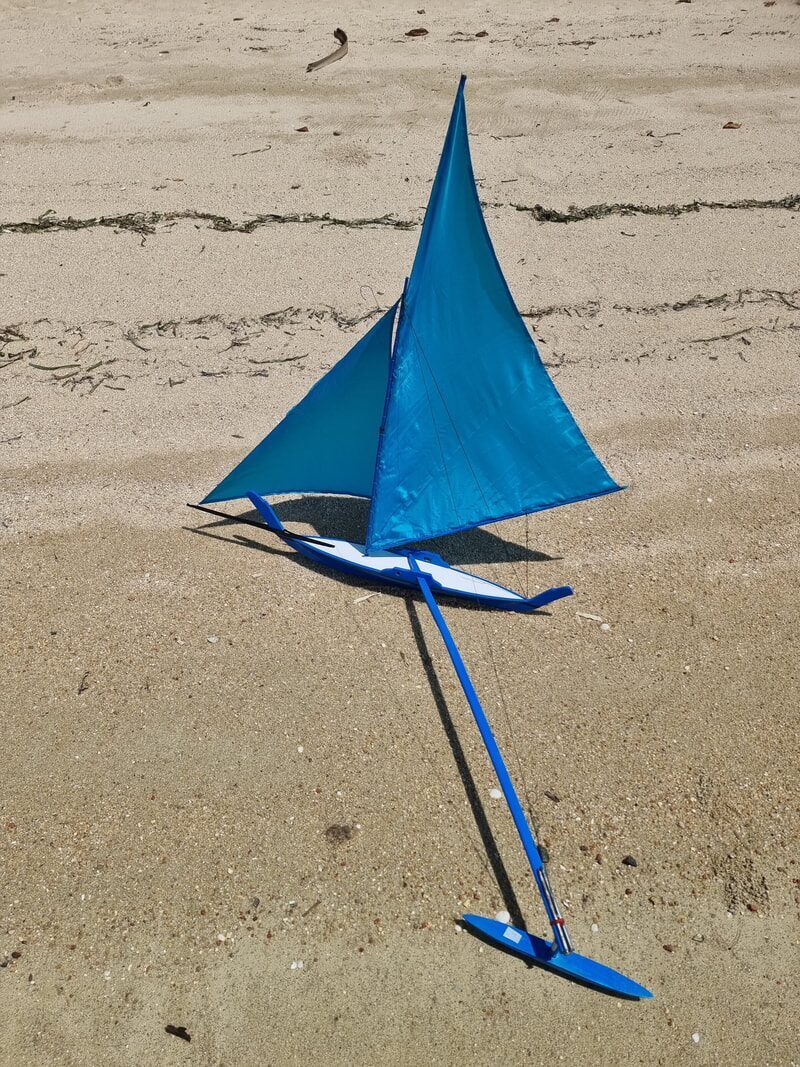 A toy jong model with teal sails and a white-and-blue hull standing on the sand
