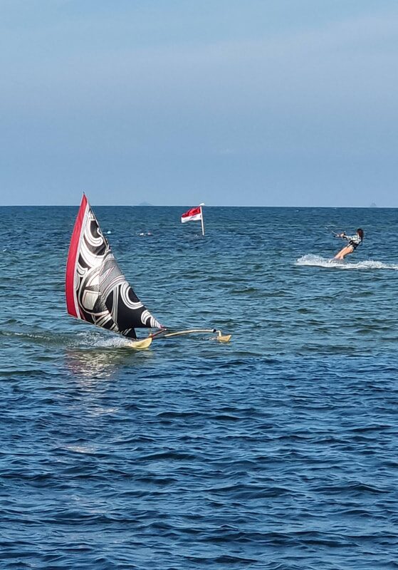 A red-sailed jong out on the water, seen from the beach