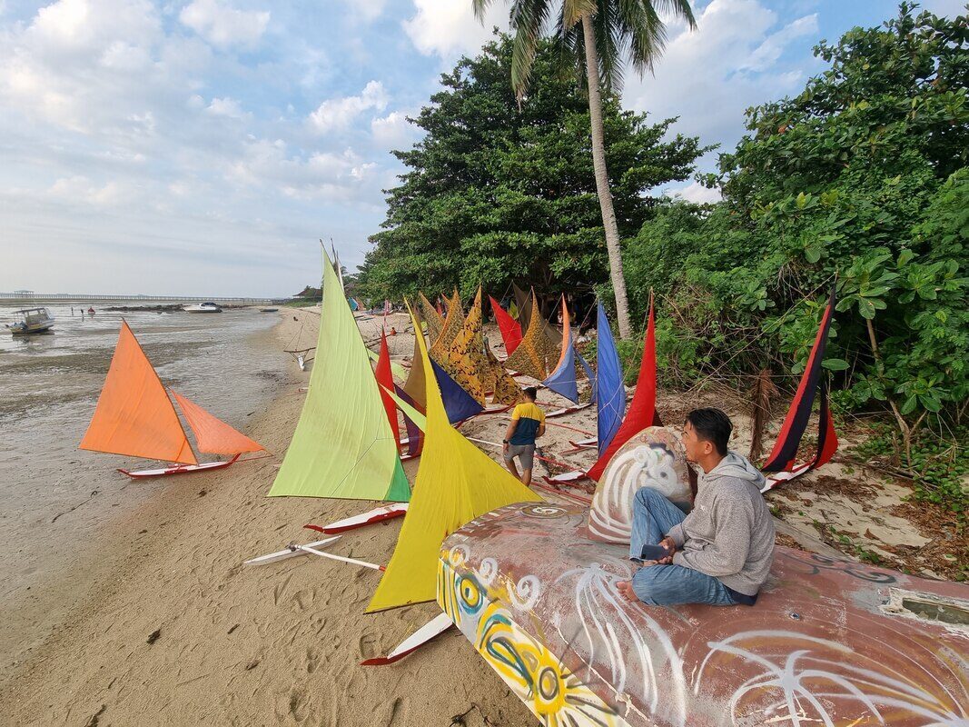 Jong sails and a boat frame propped against a beachside structure