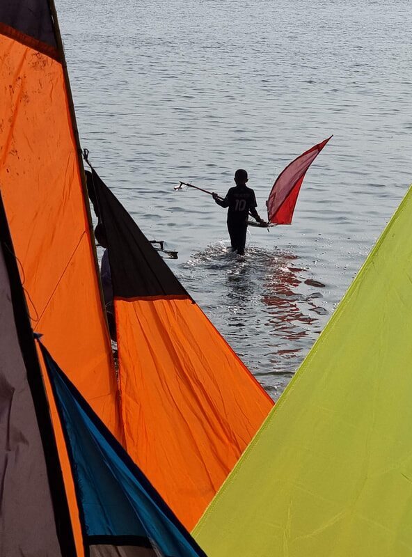 An orange-sailed jong with a figure wading into the water beside it