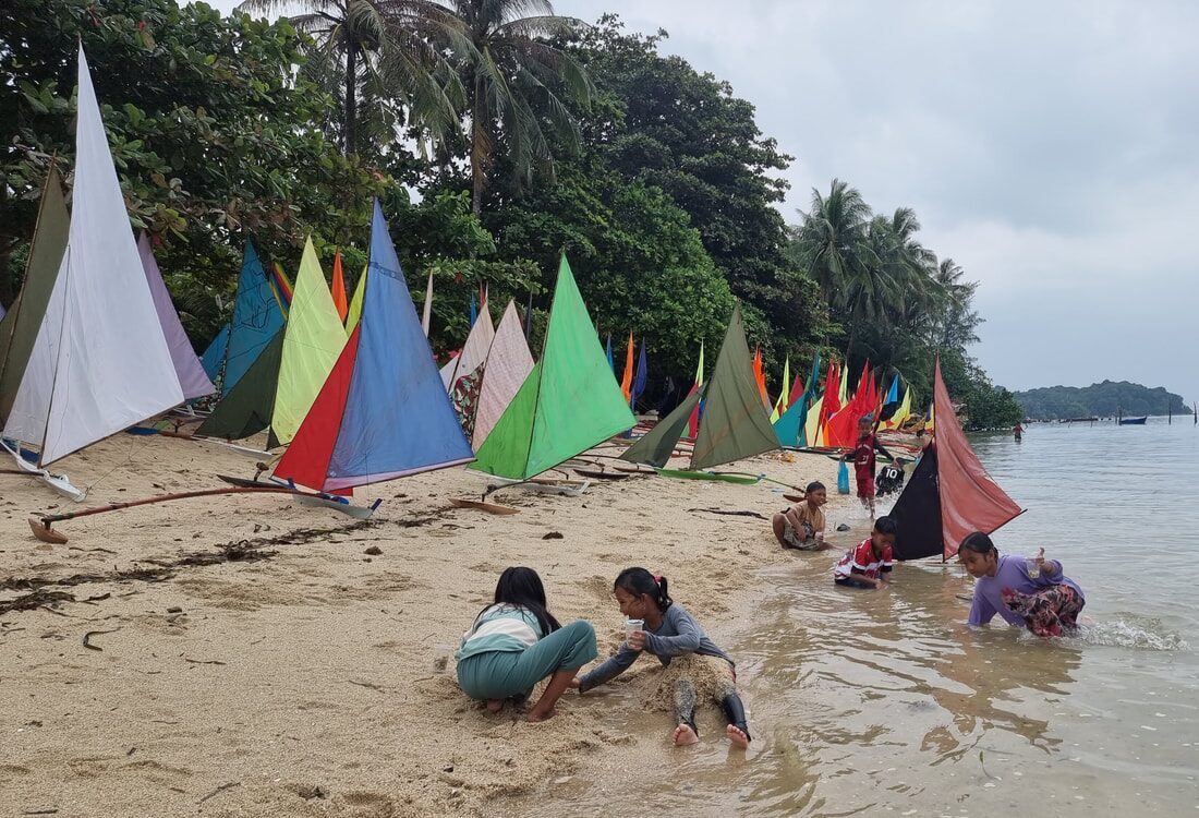 A cluster of families and kids gathered on the beach with several jongs