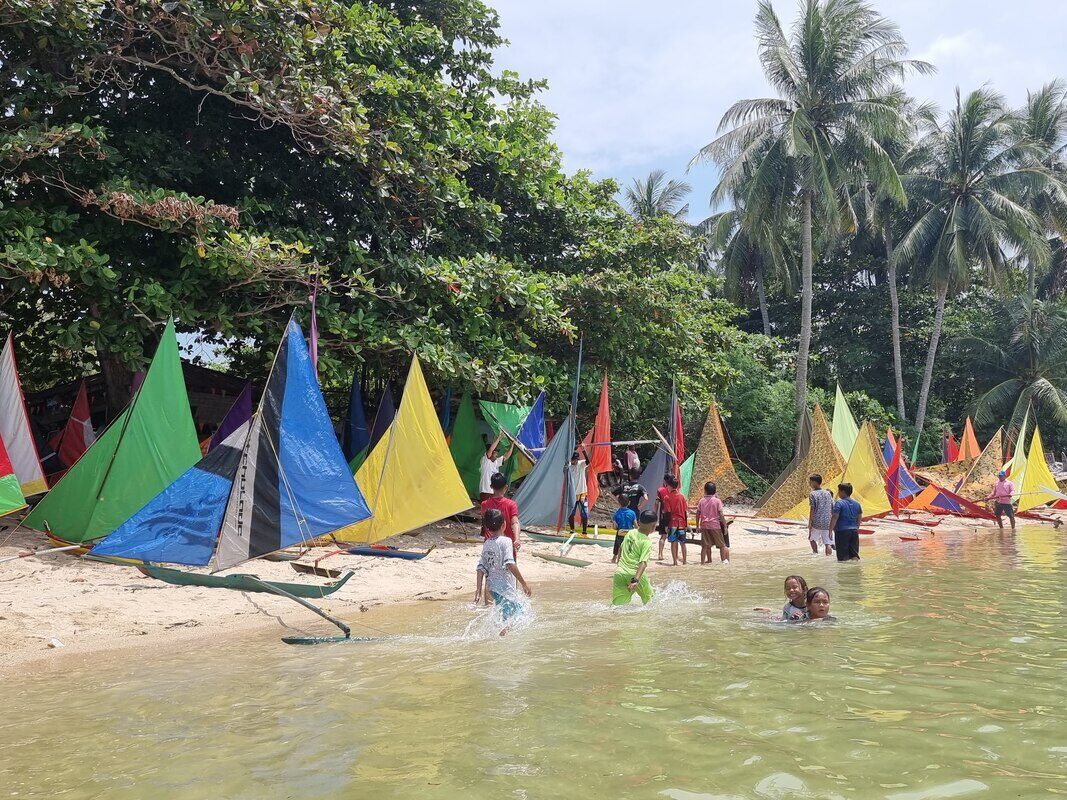 A row of colorful jongs along the shallows, kids and adults wading among them