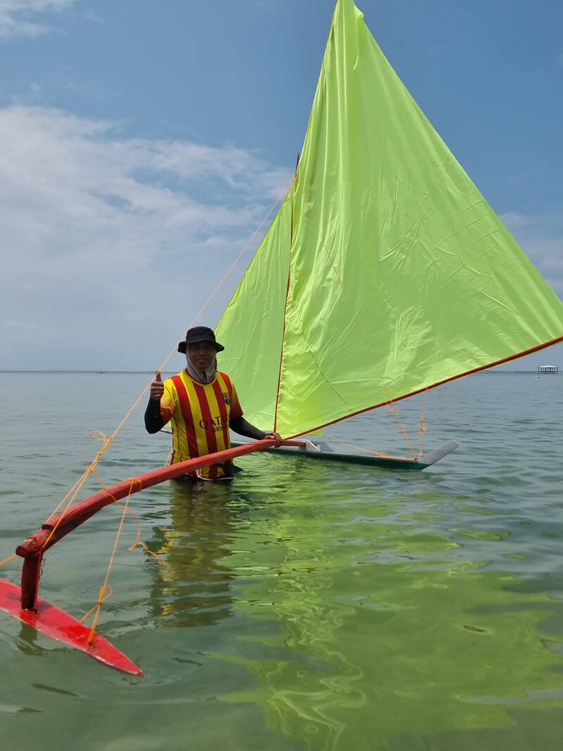 A man in a hat holding a lime-green jong sail, standing in the shallows