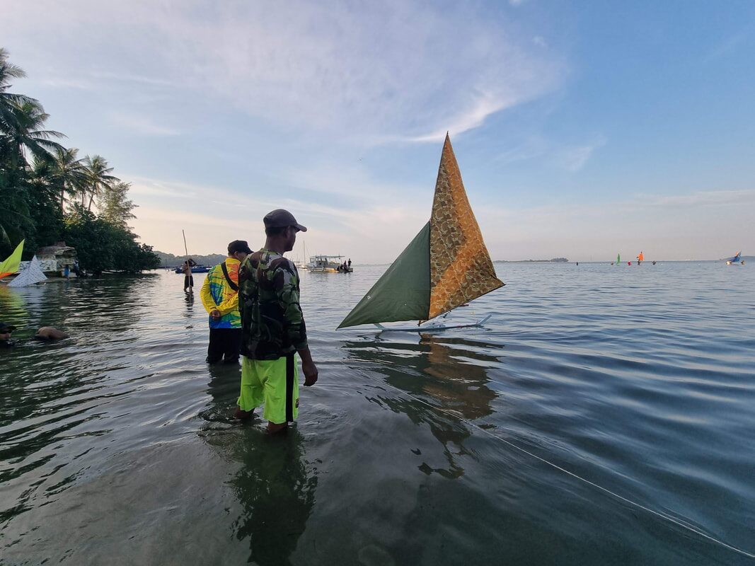 Kids wading out into the water with a yellow-sailed jong