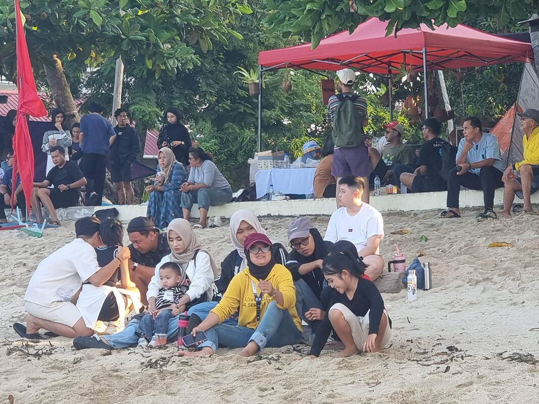 A group sitting together on the beach under a red umbrella