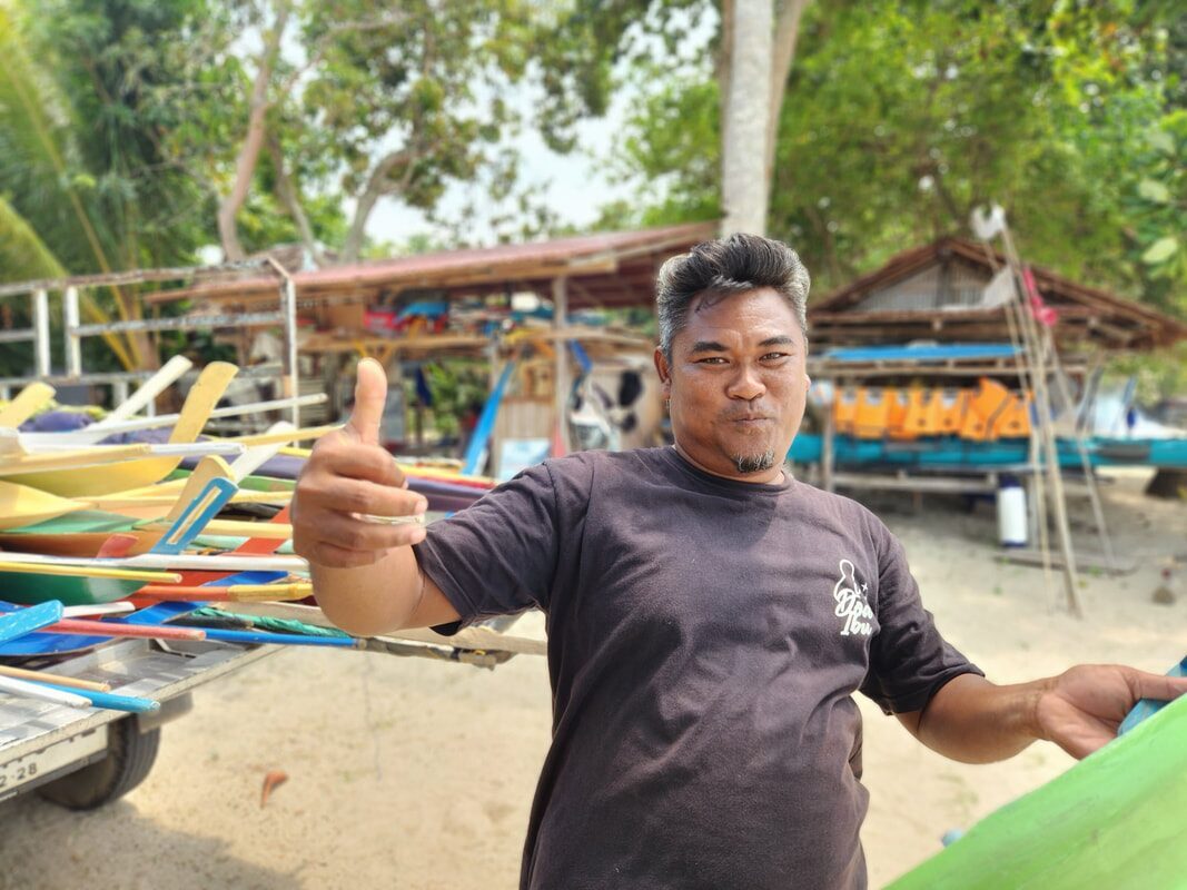 A player giving a thumbs up beside a trailer stacked with colorful jong outrigger floats