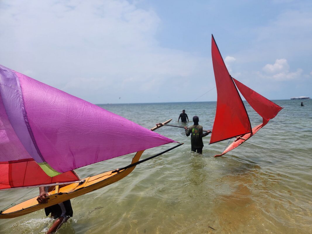 A red and multicolor jong sailing near shore, sailor wading beside it