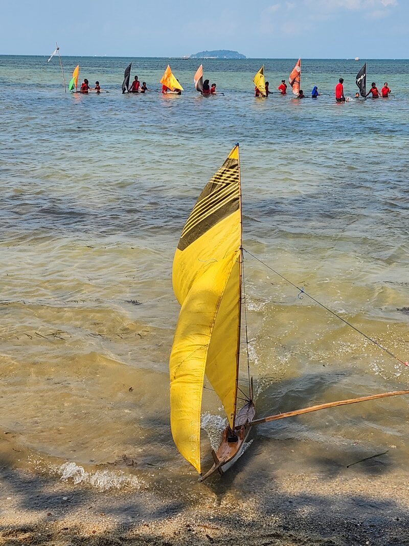 A row of jongs racing on the water, seen from the beach