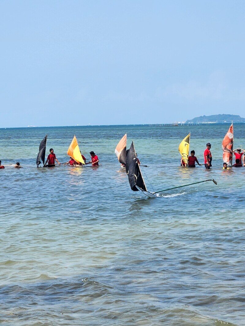 Two jongs sailing close to shore, figures wading nearby