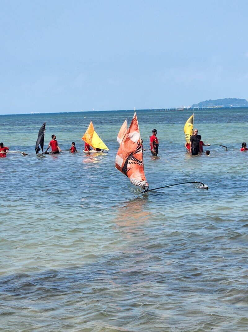 A yellow-sailed jong out on the water, seen from the shallows