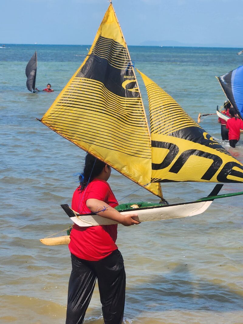 A boy holding up a yellow-sailed jong, smiling