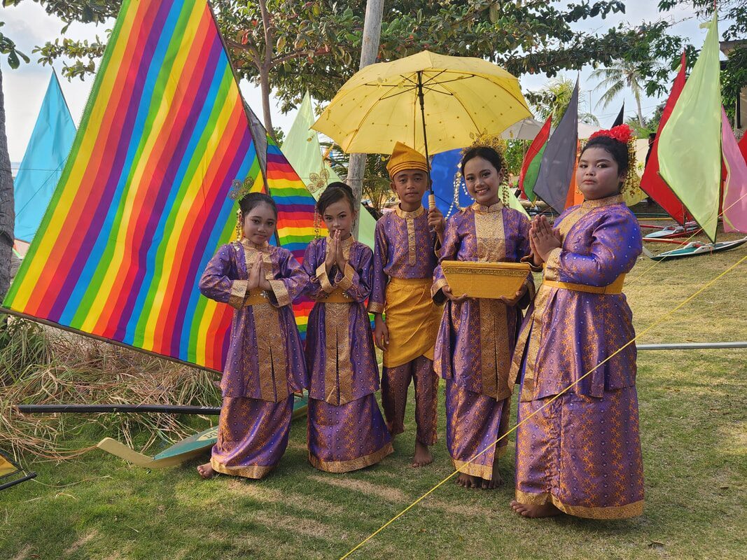 A group of performers in colorful traditional dress holding an umbrella and decorations