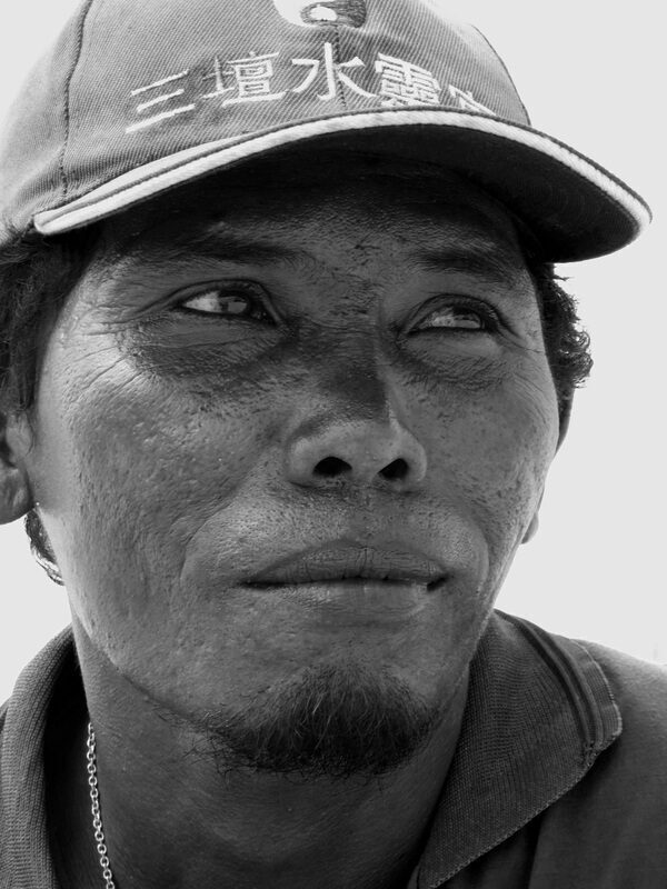 Close-up black-and-white portrait of a weathered fisherman in a cap, looking off to the side