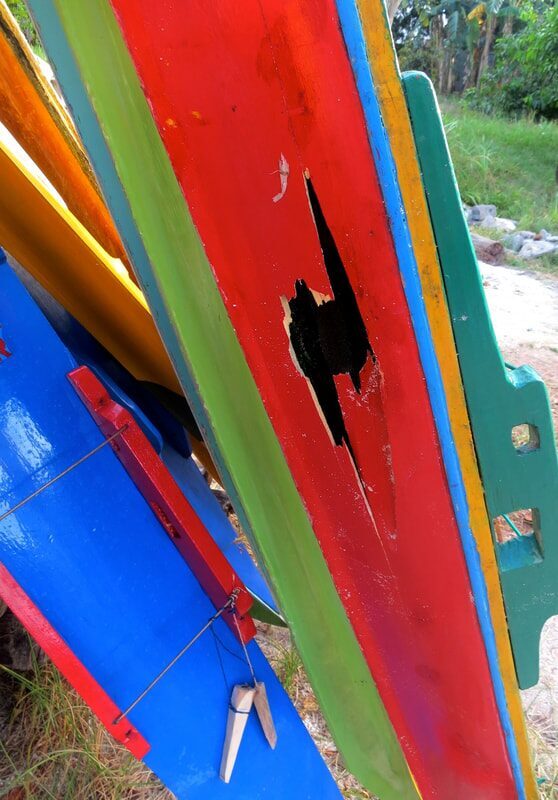 Close-up of stacked jong sail boards in red, green, blue and yellow, one with a chunk of paint and wood broken away