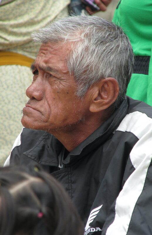 Close portrait of an older man with grey hair watching the race, a child's hair visible in the foreground