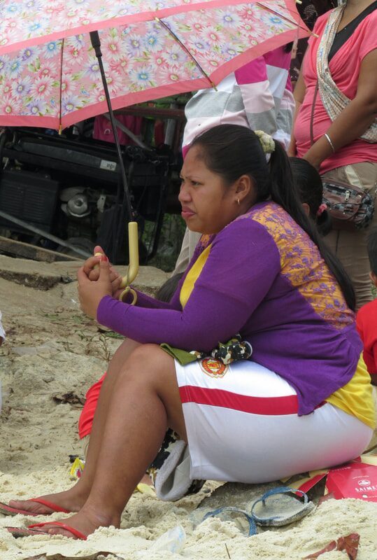A woman sheltering under a pink floral umbrella on the beach, watching the race