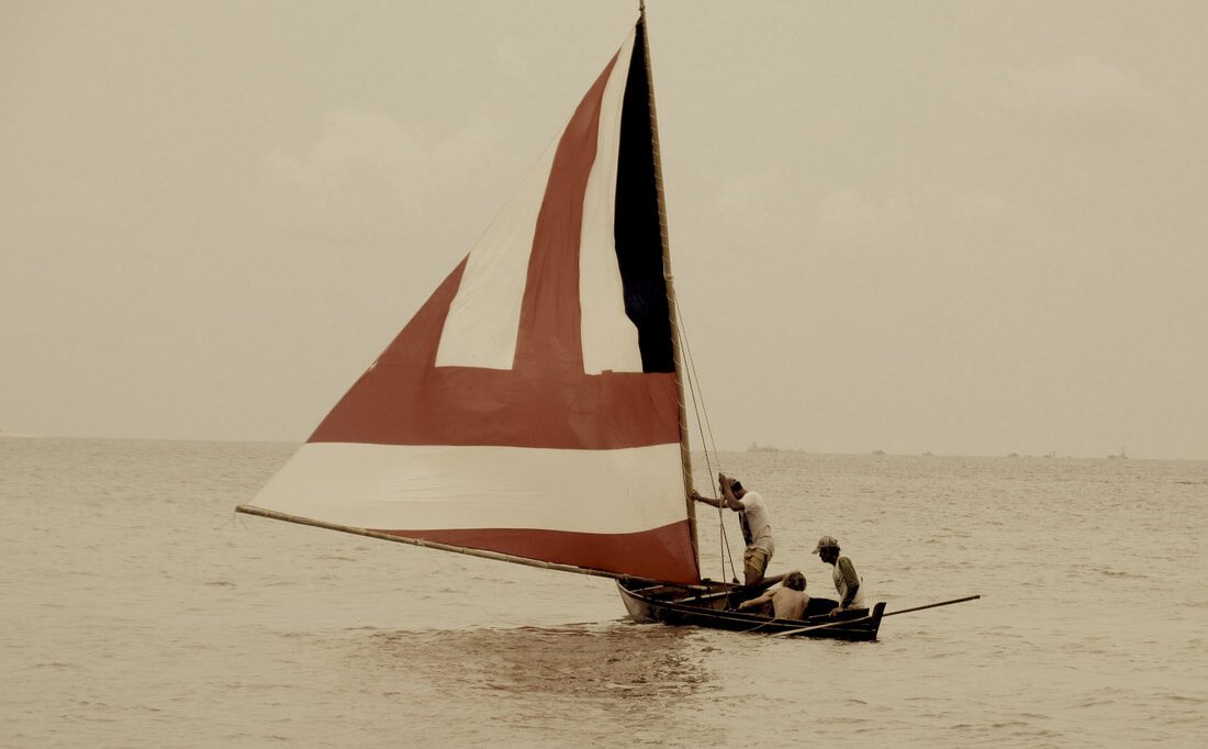 Sepia photo of a red-and-white sampan layar under sail, three crew aboard on calm water
