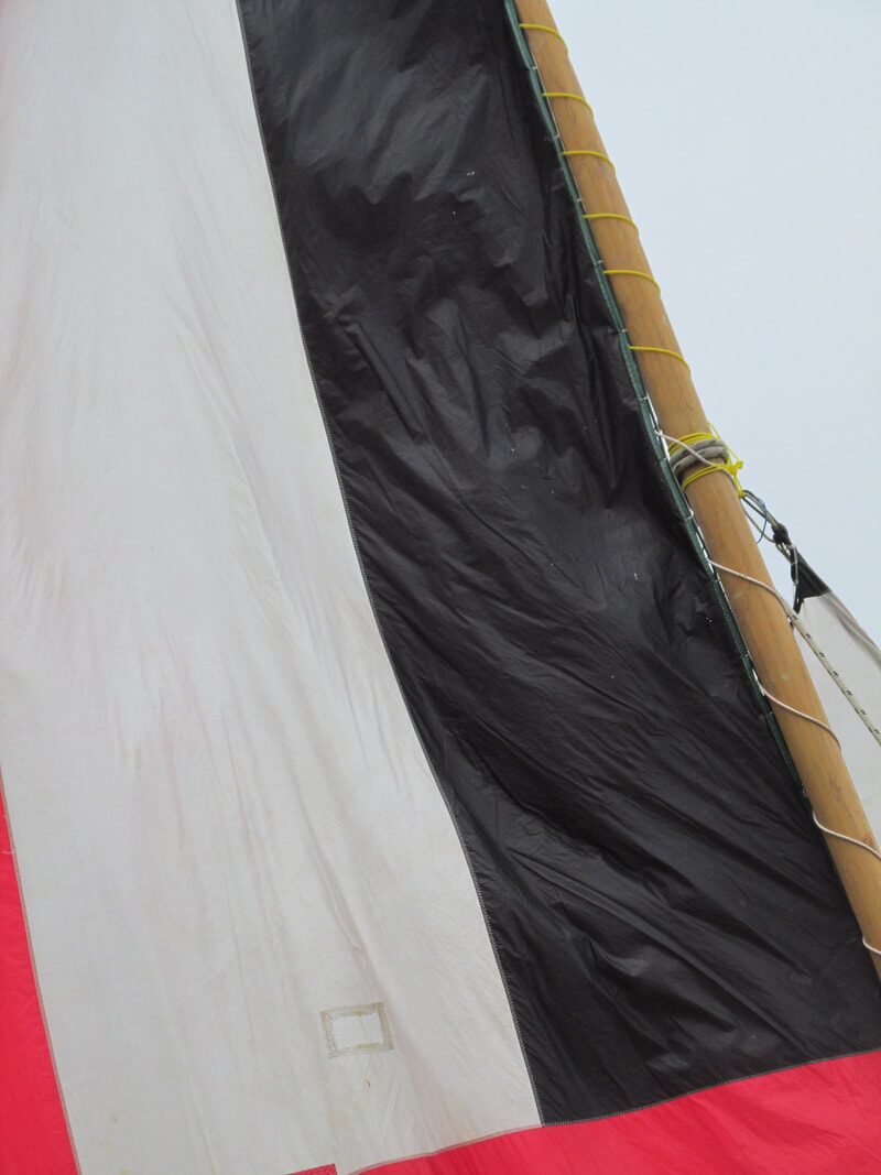 Close-up of a sampan layar's red, white and black sail cloth against its wooden mast