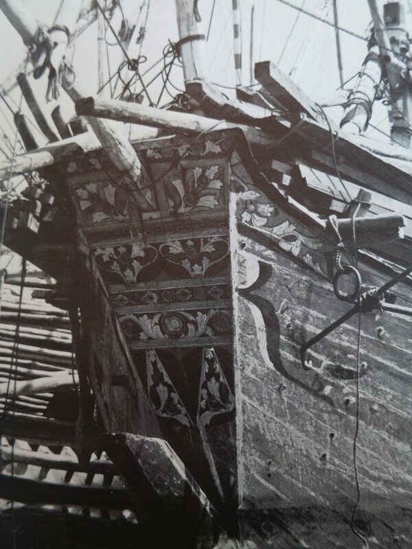 Close-up of an ornately carved wooden ship's bow, floral relief carving on old timber