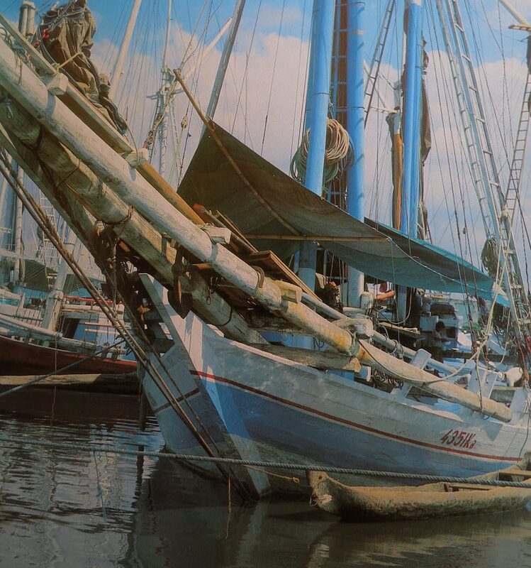 Color archival photo of large wooden cargo schooners moored bow-to-bow in a harbor, tarpaulins rigged over the deck