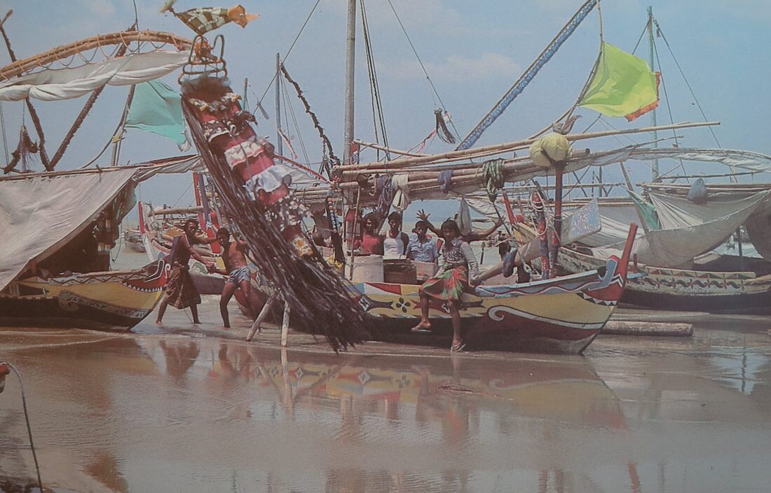 Color photo of a brightly painted, ornately decorated boat on the beach, kids climbing its high curved prow