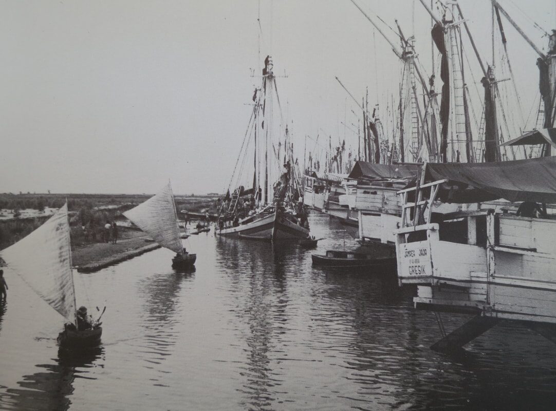 Black-and-white archival photo of a canal crowded with tall-masted cargo boats, labeled 'Gresik'