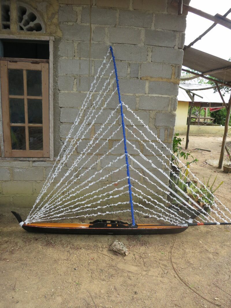 A finished jong hull with a full rigged white sail leaning against a brick house wall