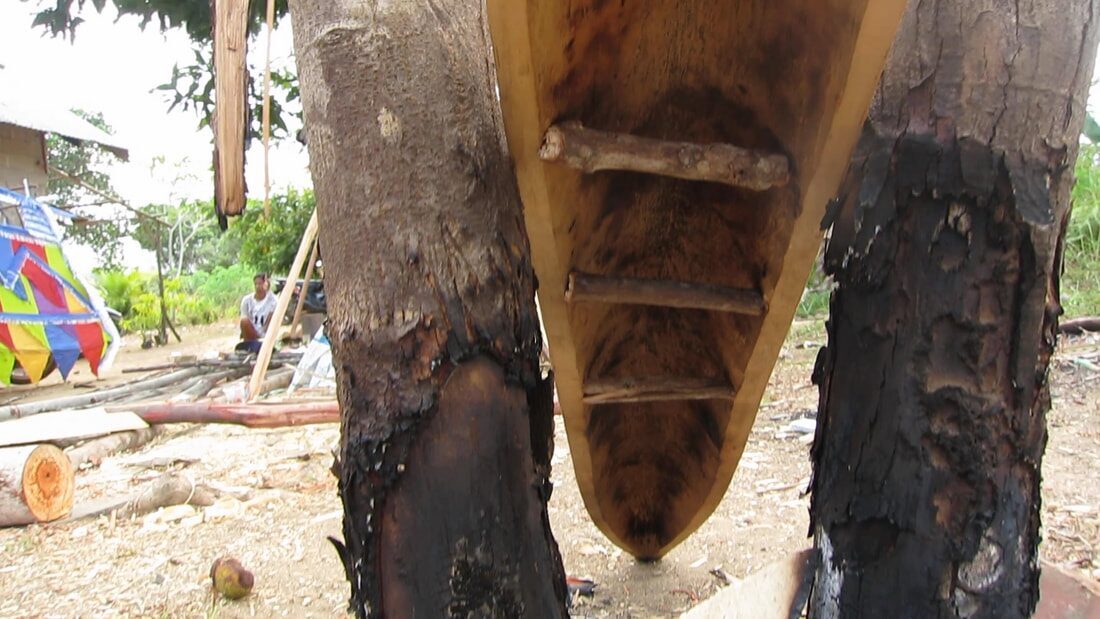 Looking down into a carved jong hull's hollow interior with wooden ribs, colorful sails and a seated man visible in the background
