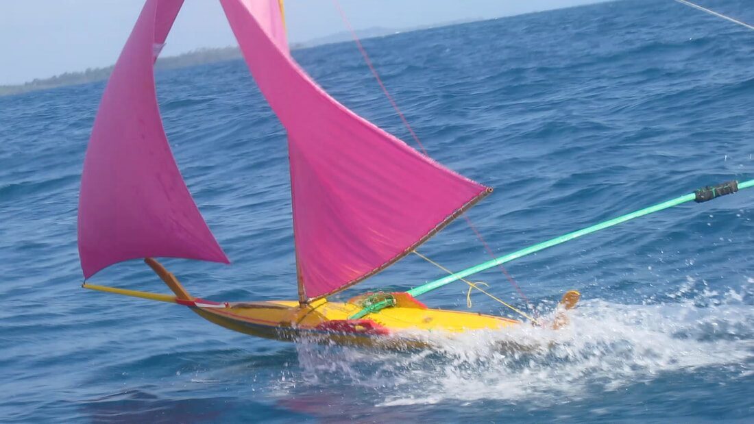 Close view of a yellow-hulled jong with pink sails cutting through the water at speed