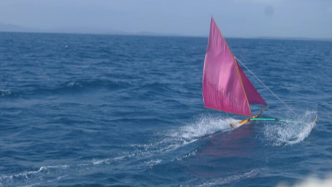 A jong with a bright pink sail heeling hard and throwing spray as it races across open water