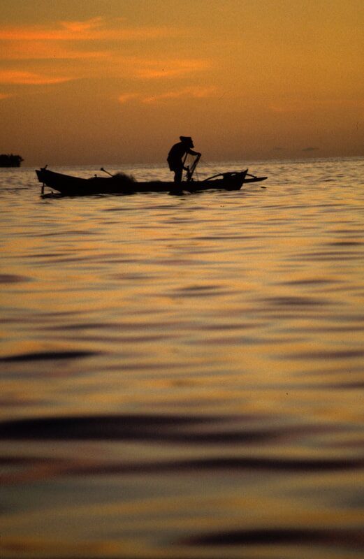Archival silhouette of a fisherman working aboard his boat at sunset, warm orange sky reflected on the water